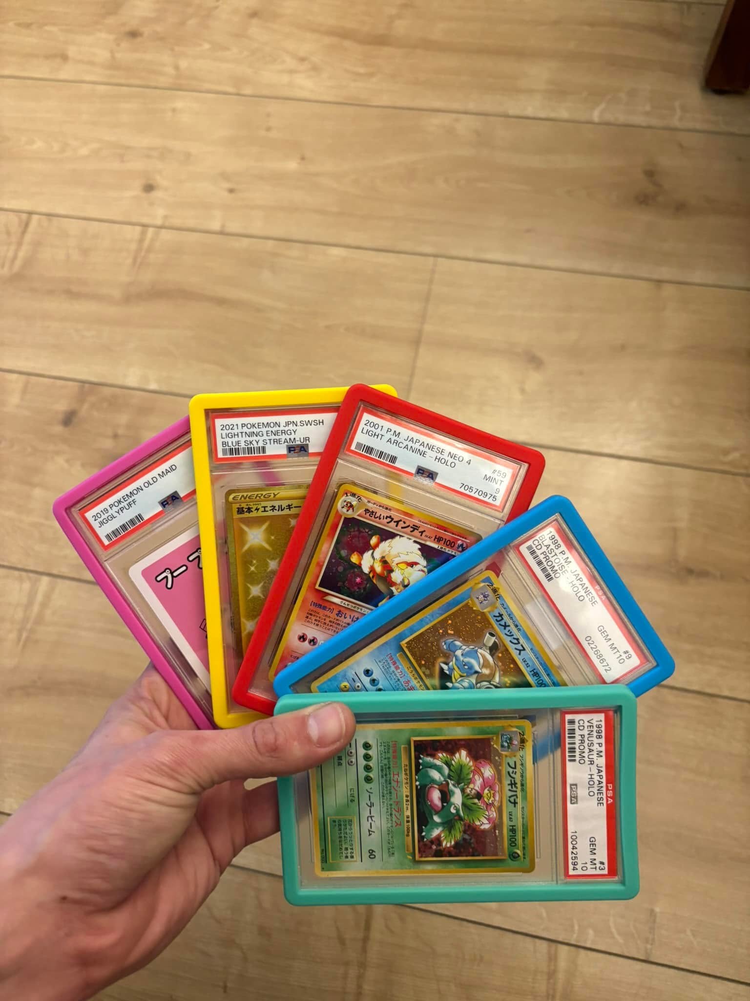 Hand holding five PSA slabs each wearing a different color Slab Guard bumper